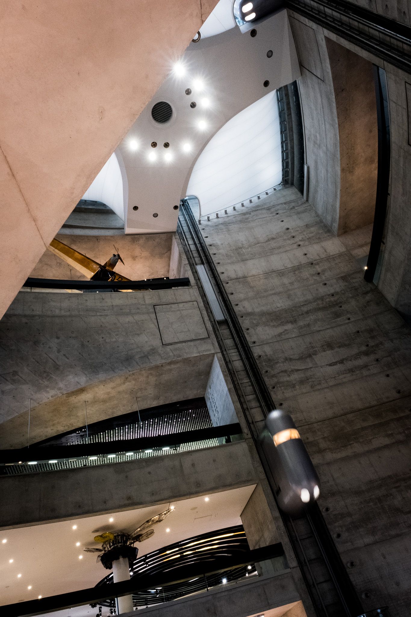 Modern architectural interior with concrete walls, glass elevator shaft, and dramatic multi-level atrium lighting.