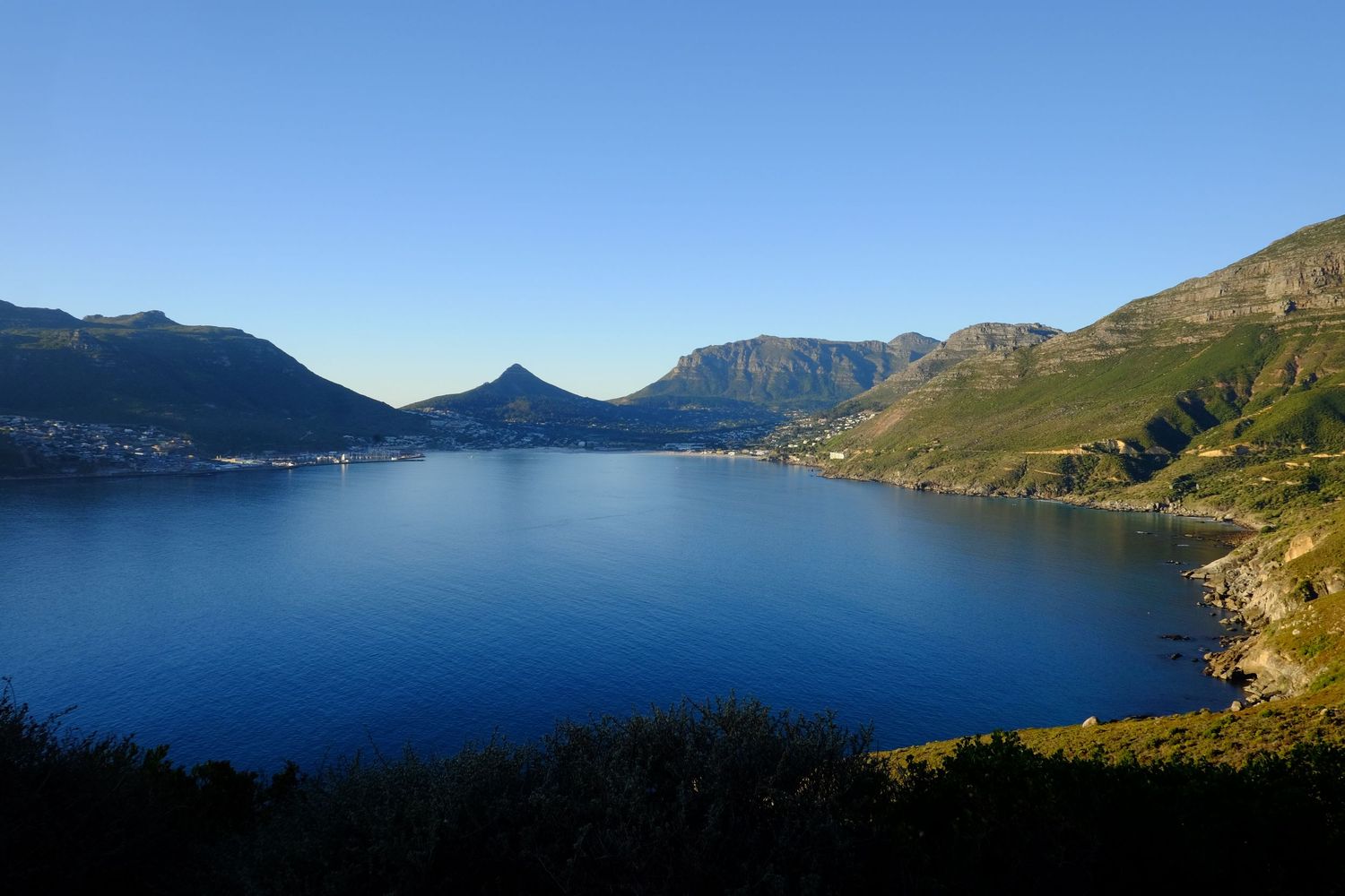 Panoramic view of a serene blue bay surrounded by mountains in Hout Bay, Cape Town, South Africa.