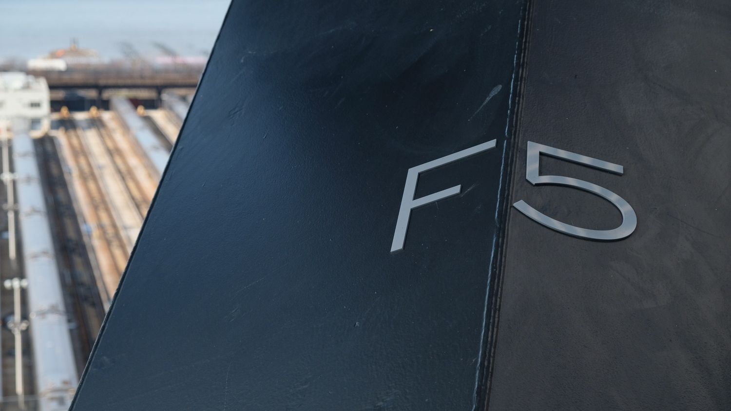 Close-up of an F5 label on a dark metallic surface with railway tracks visible in the background.