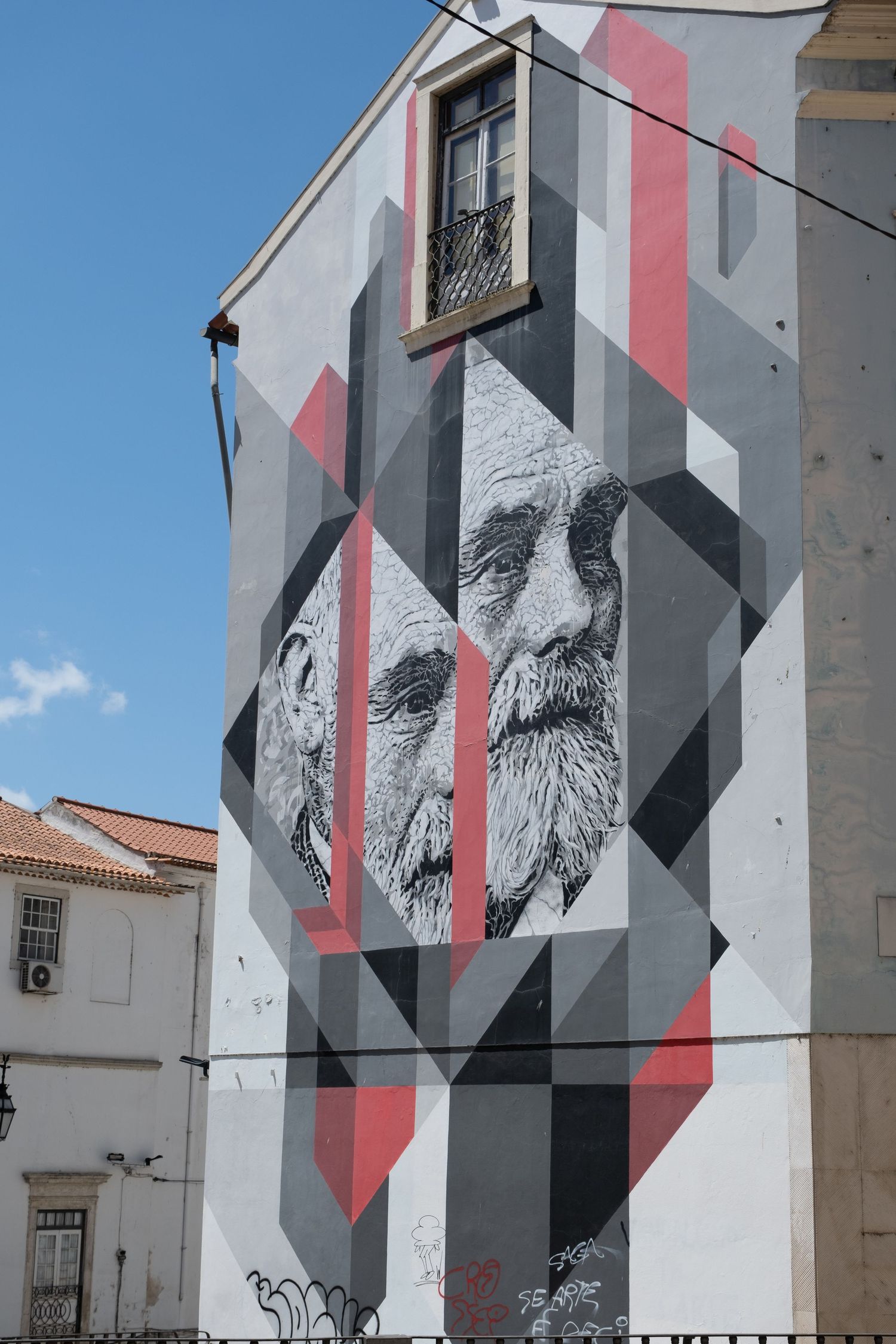 Large street art mural of two elderly bearded men on geometric gray and red building facade.
