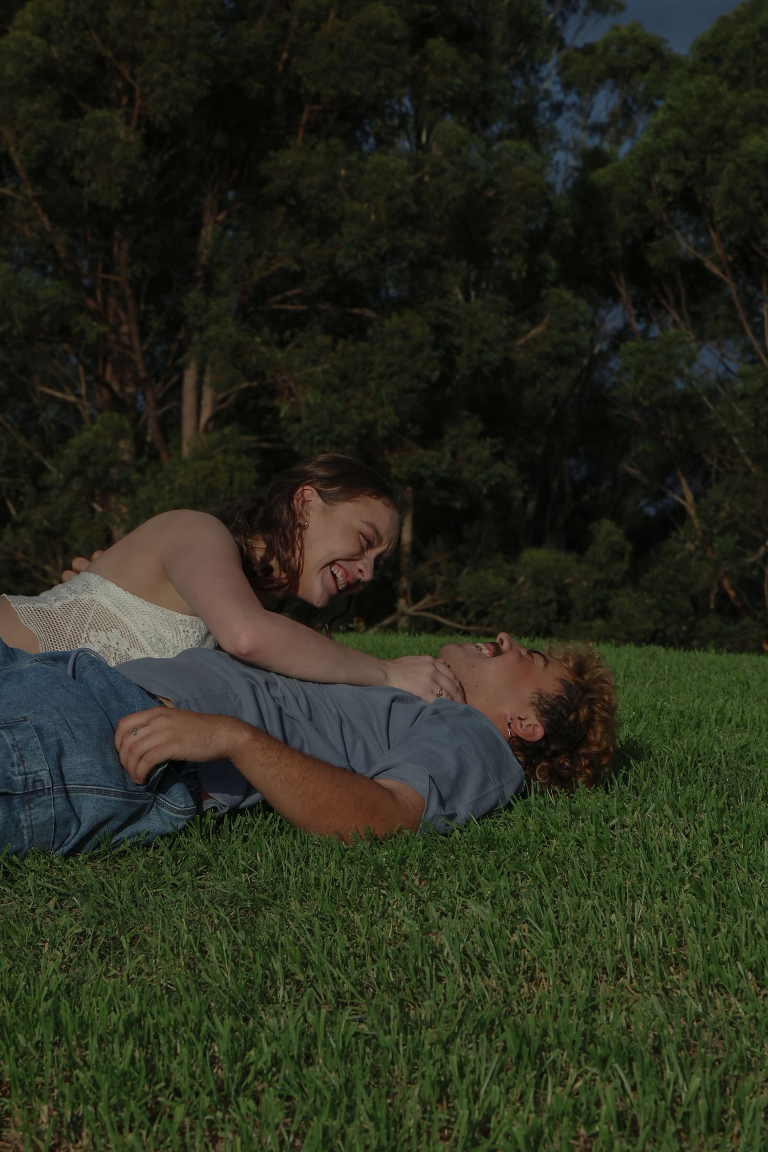 A couple laying on the grass together and smiling at each other with love in their eyes