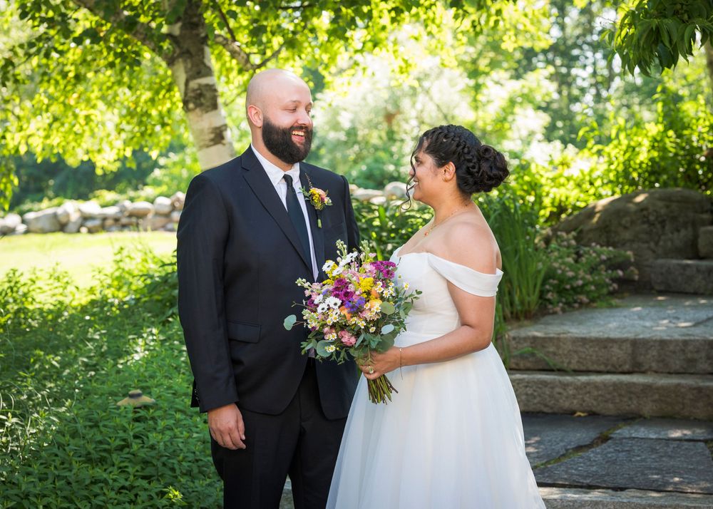 Bride and groom share a romantic moment outdoors, bride holding colorful bouquet in white off-shoulder gown.