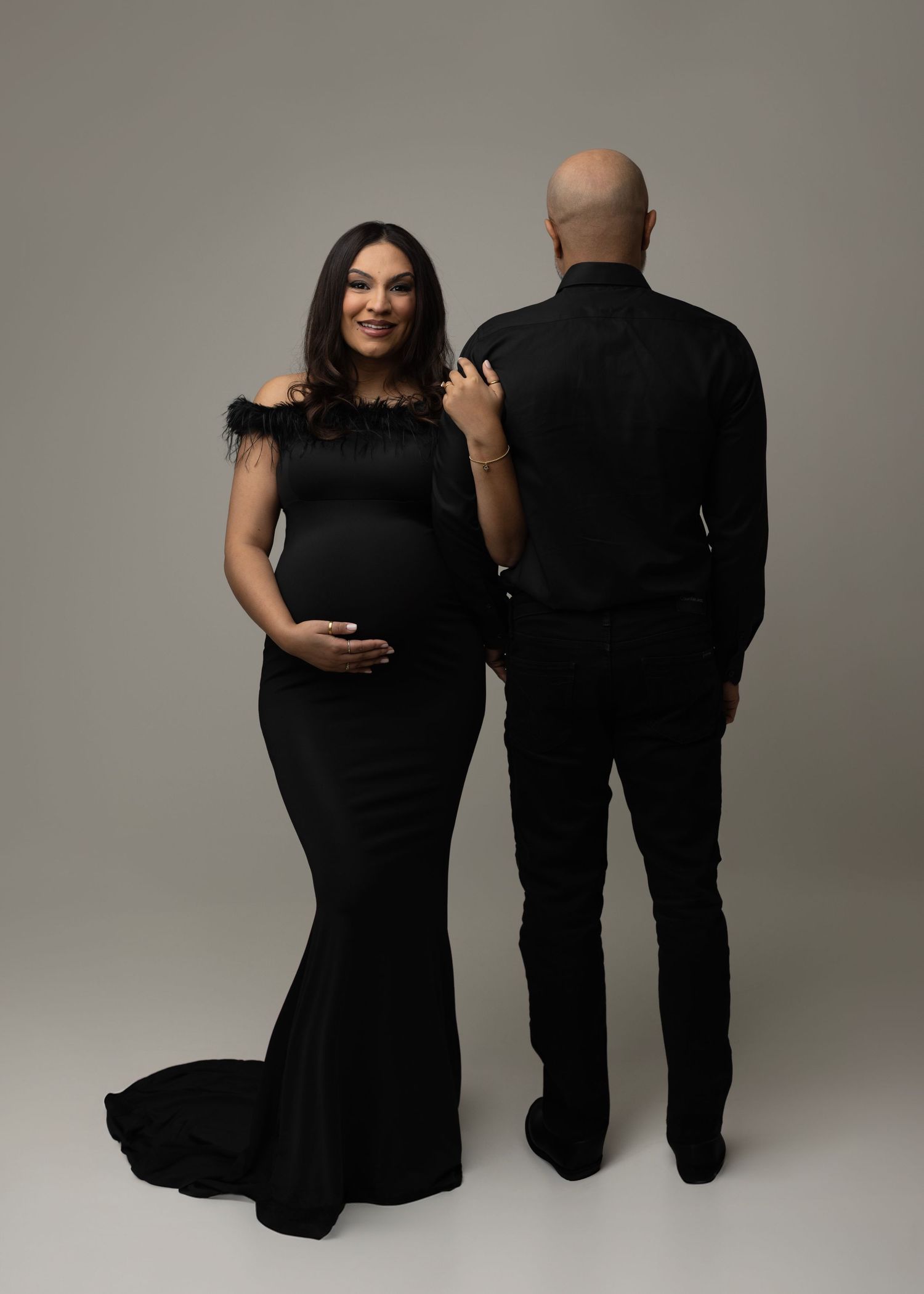 A series of intimate maternity photos showing a couple in black outfits against a neutral gray backdrop. Elizabeth Lang Photography Surrey