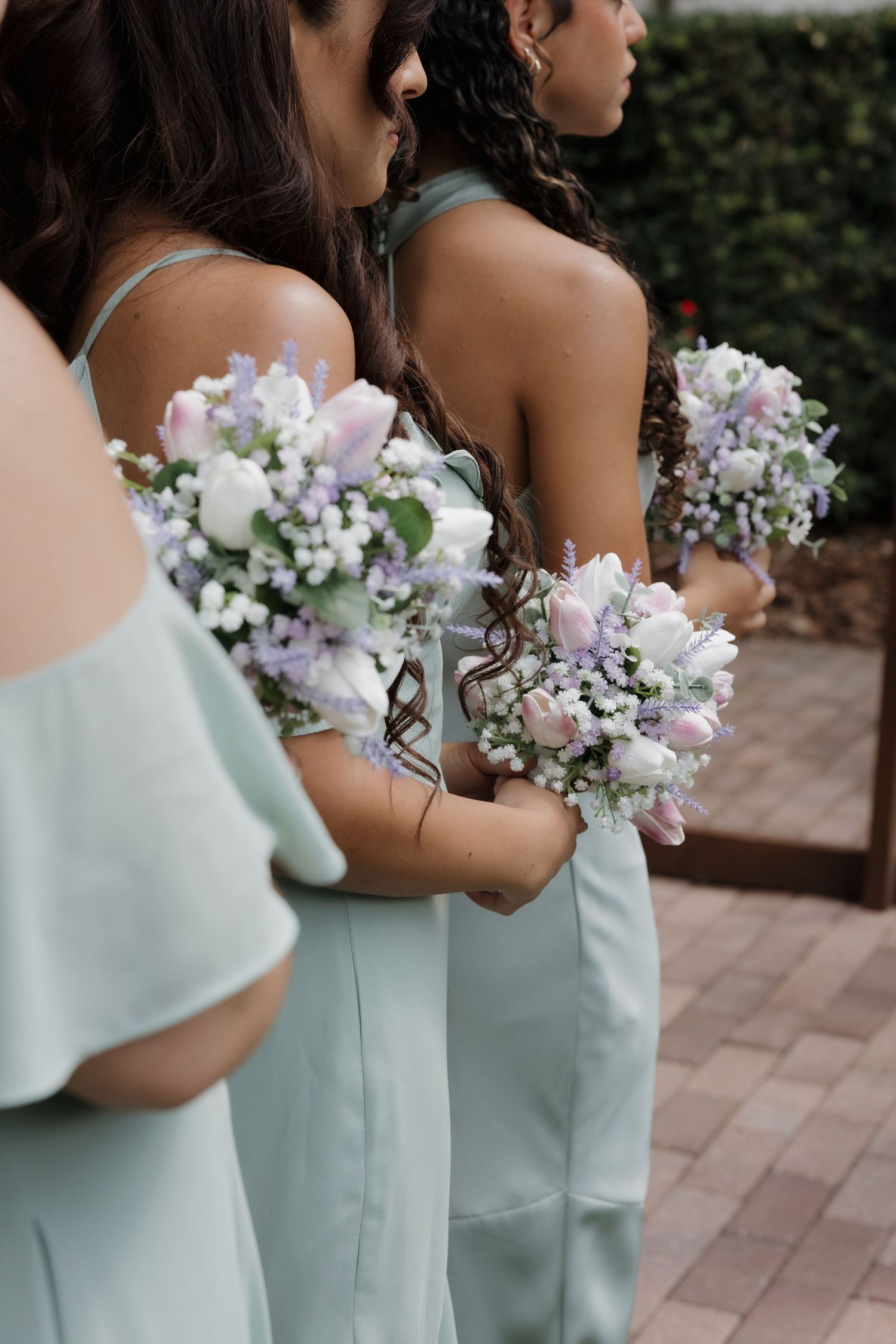Bridesmaids in sage green dresses holding matching bouquets of tulips, lavender, and baby's breath.