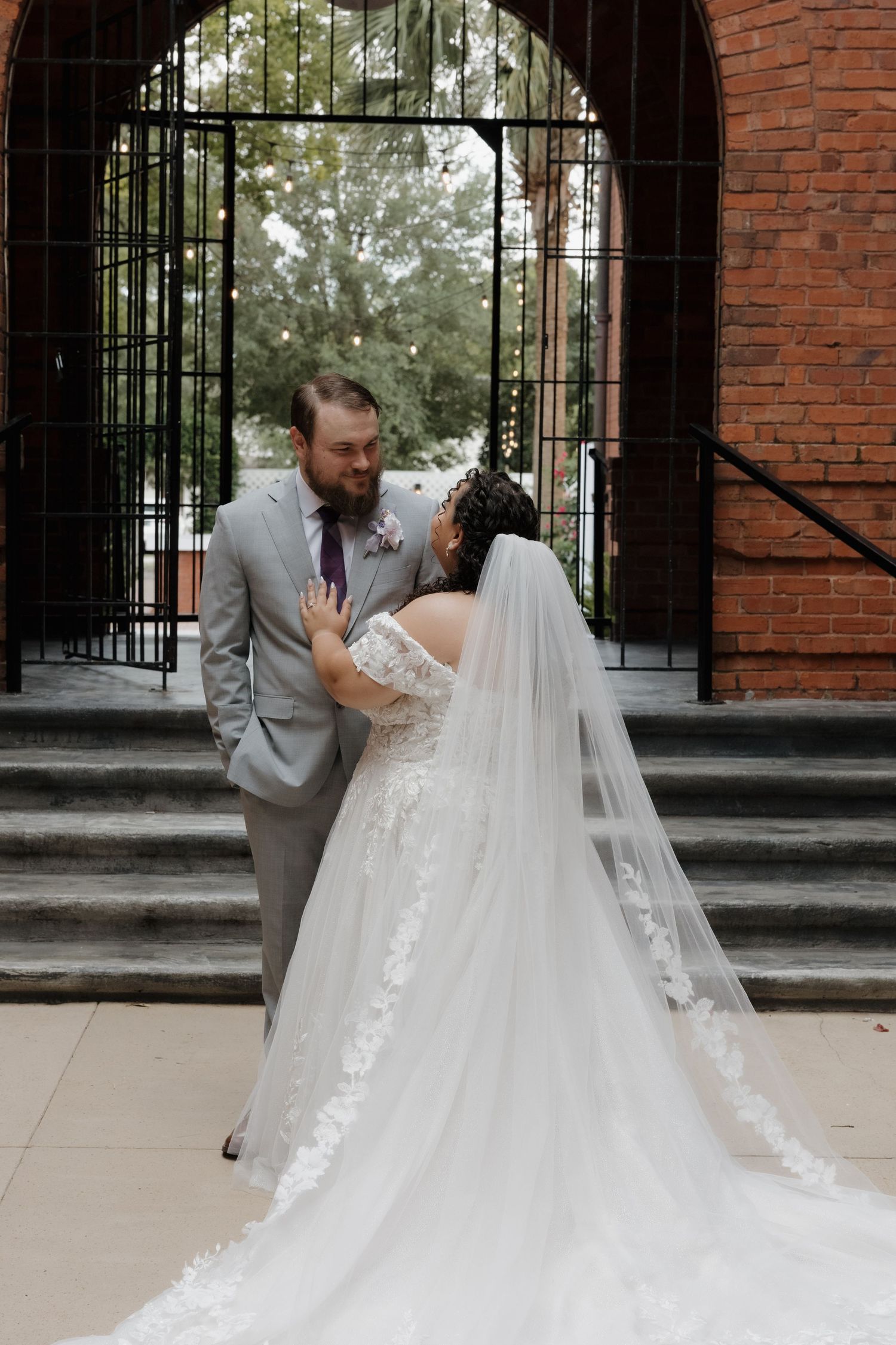 Bride and groom share romantic moment under iron arch at brick building wedding venue.
