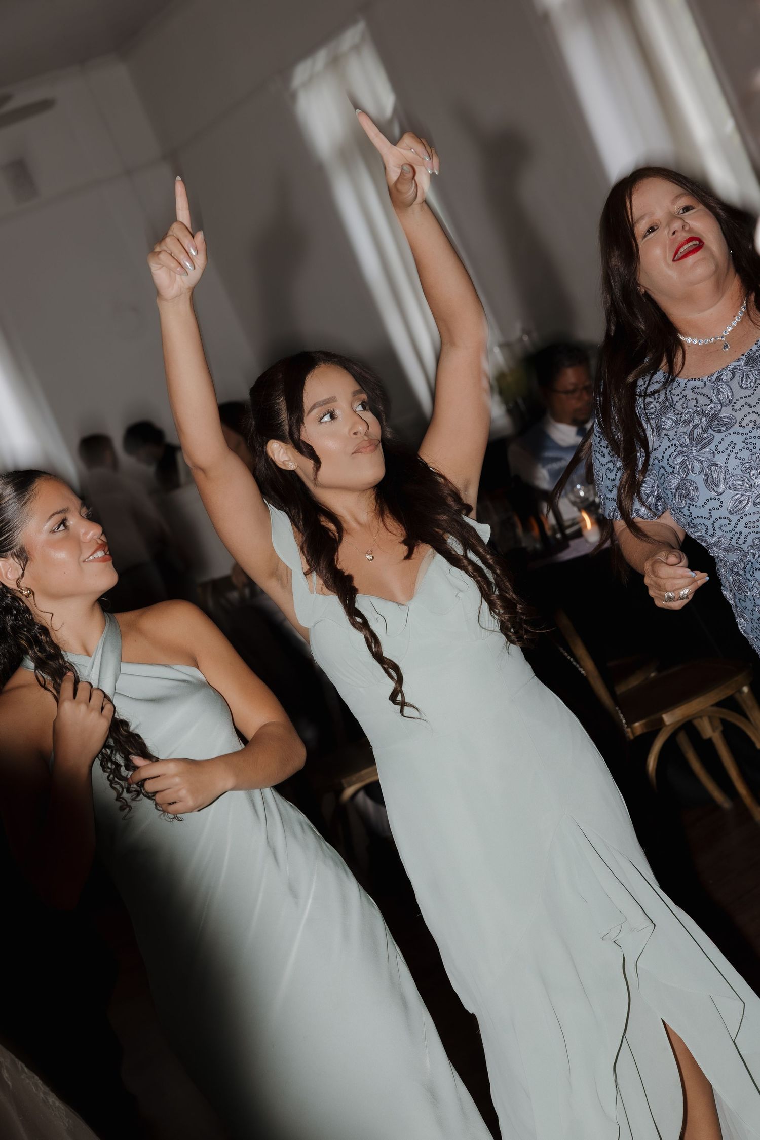 Bridesmaids in mint green dresses dancing joyfully at a wedding reception, with one raising her arms up.