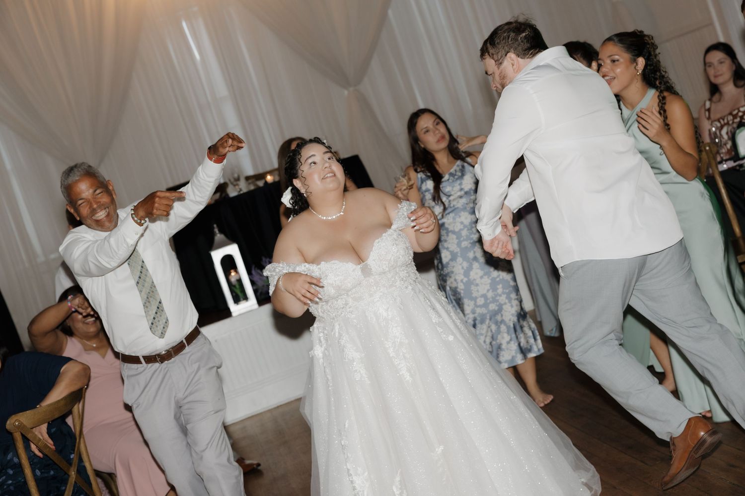 Bride and groom dancing joyfully with guests at a lively wedding reception celebration.