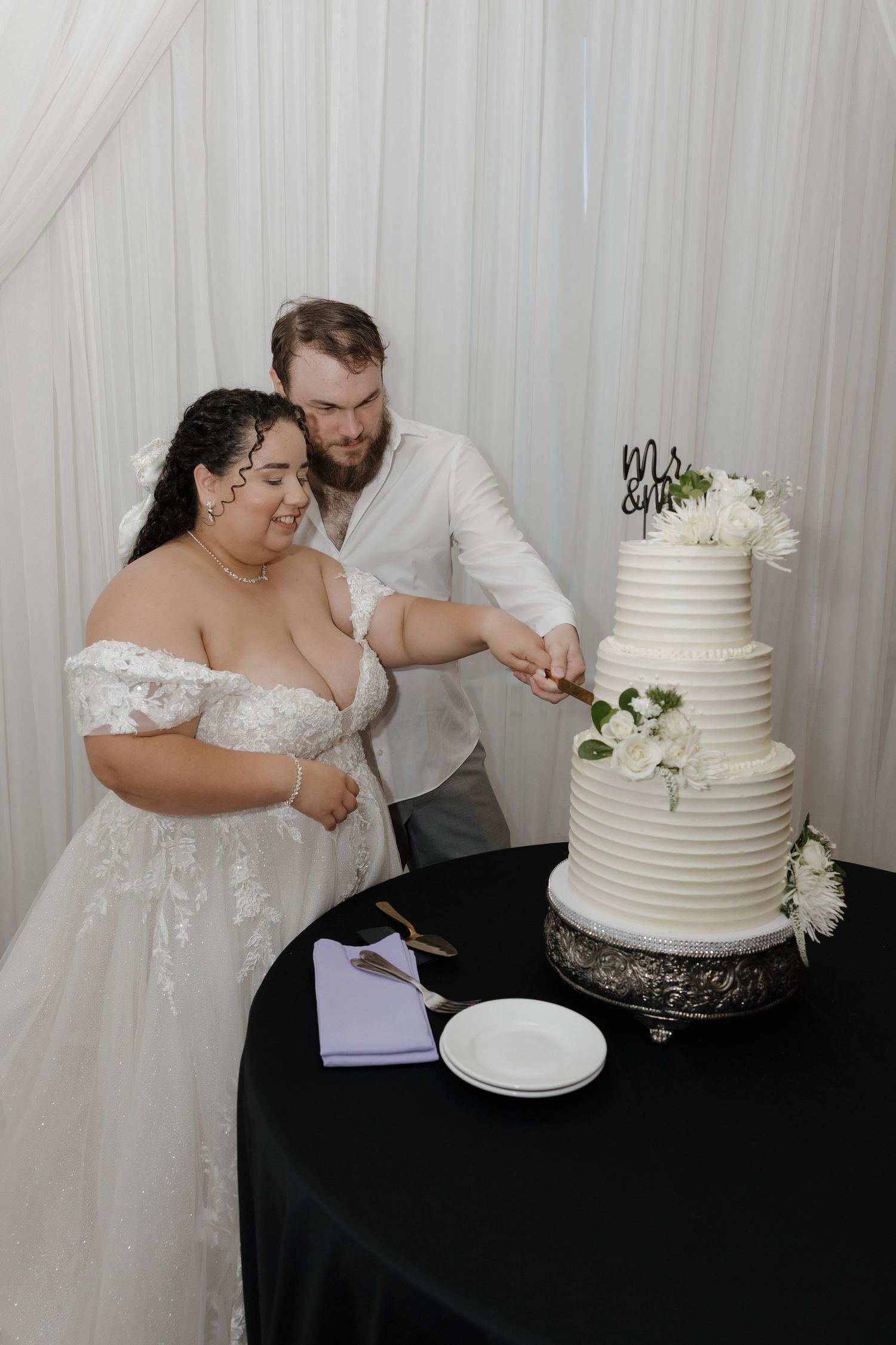 Bride and groom cutting a four-tier white wedding cake decorated with flowers and a Mrs & Mrs topper.