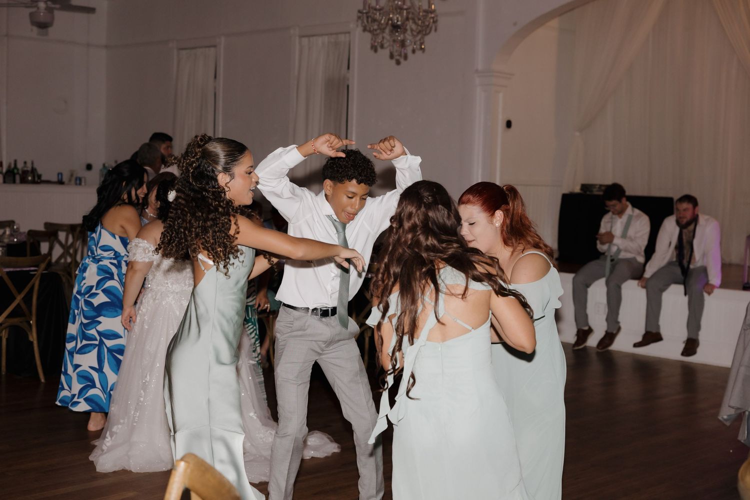 Wedding guests dancing joyfully together on a decorated ballroom dance floor during a lively wedding reception.