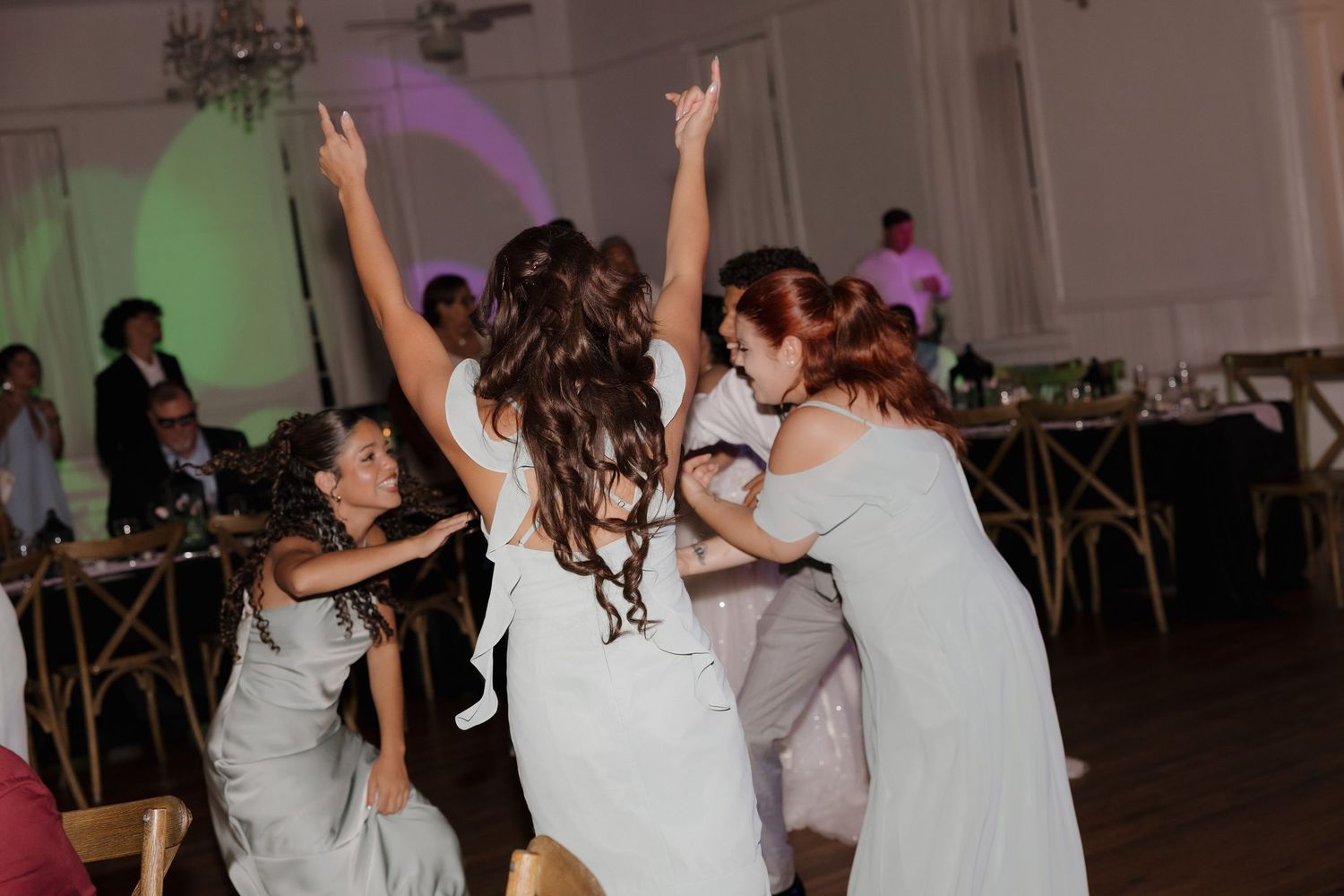 Bride and bridesmaids dancing joyfully at a wedding reception in an elegant ballroom.