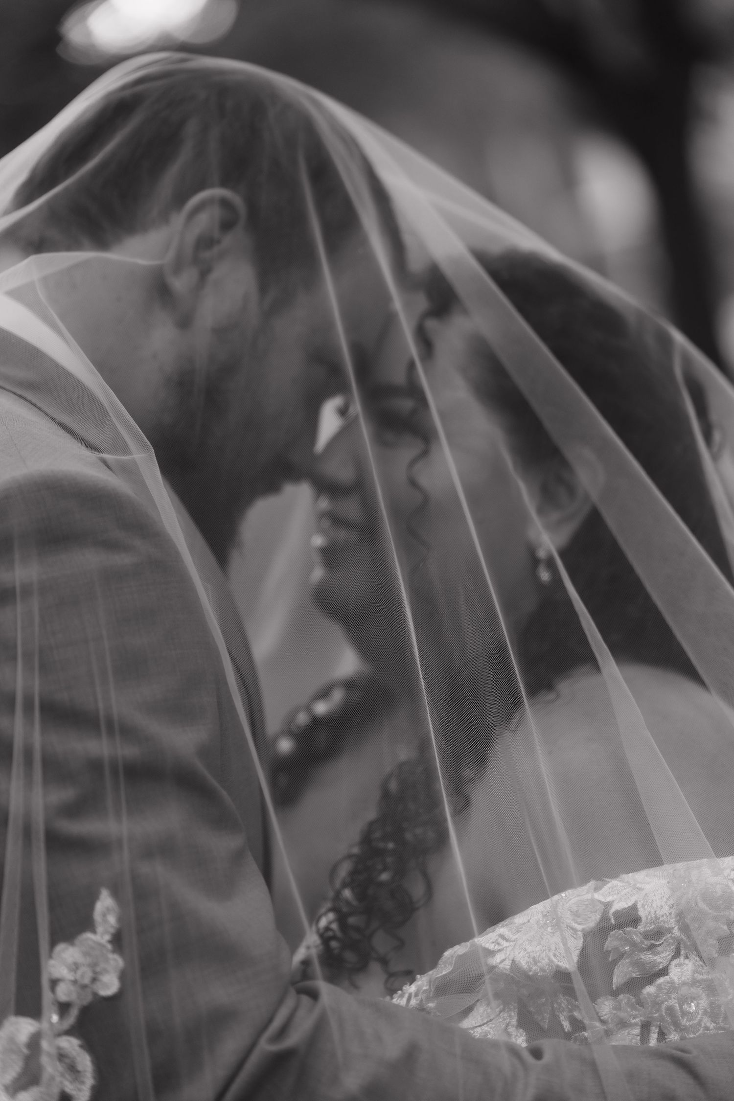 Romantic black and white photo of bride and groom sharing intimate moment under wedding veil.