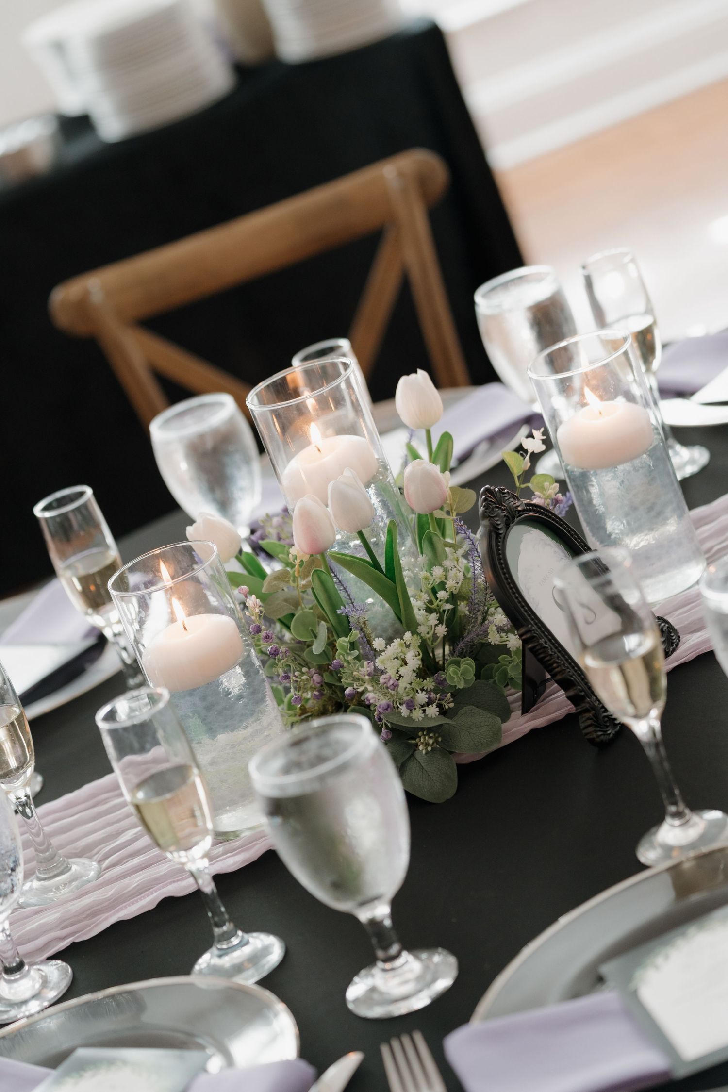 Elegant wedding reception table with white tulips, candles, champagne flutes, and black tablecloth centerpiece decor.