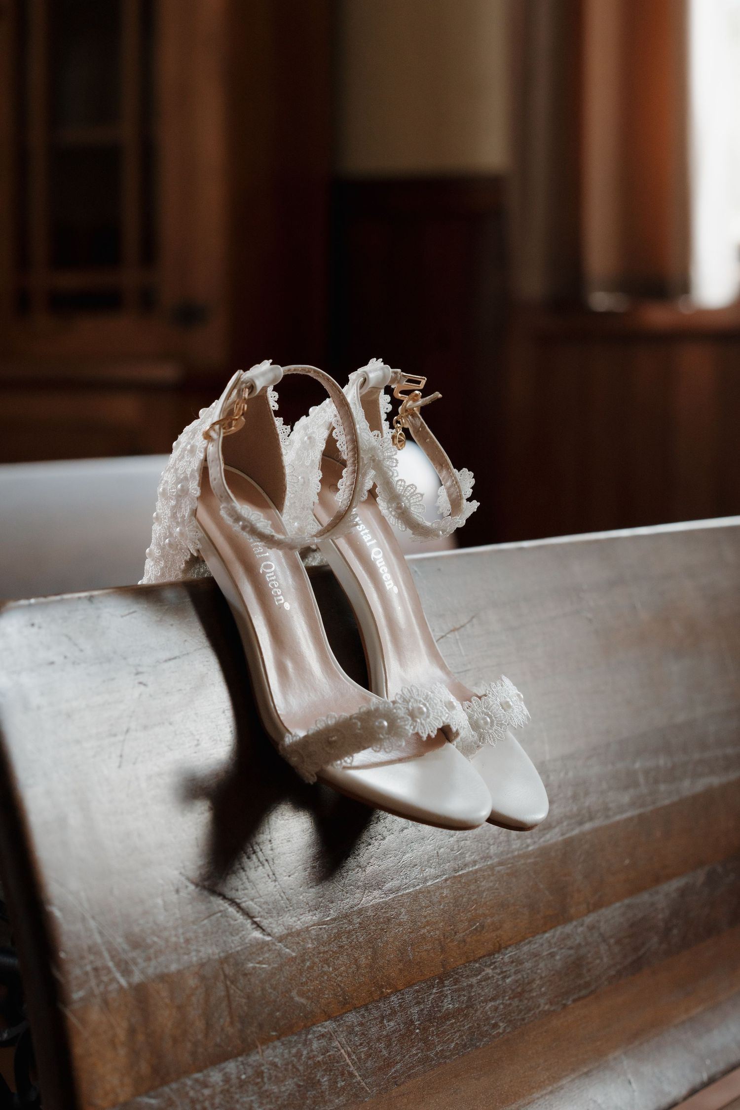 Elegant white bridal heels with lace details resting on a wooden church pew.