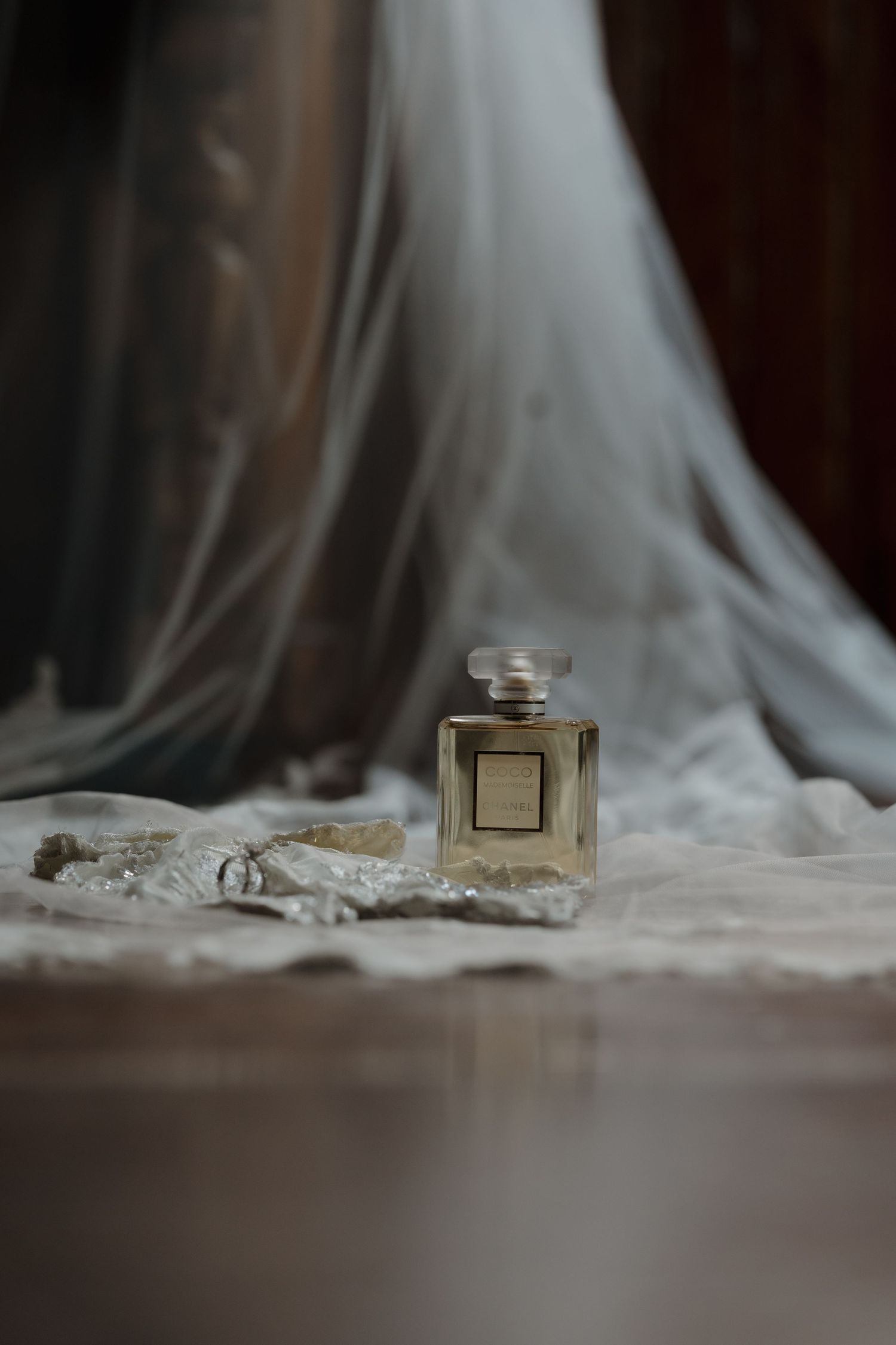 Chanel perfume bottle with bridal accessories on white lace fabric with veil backdrop.