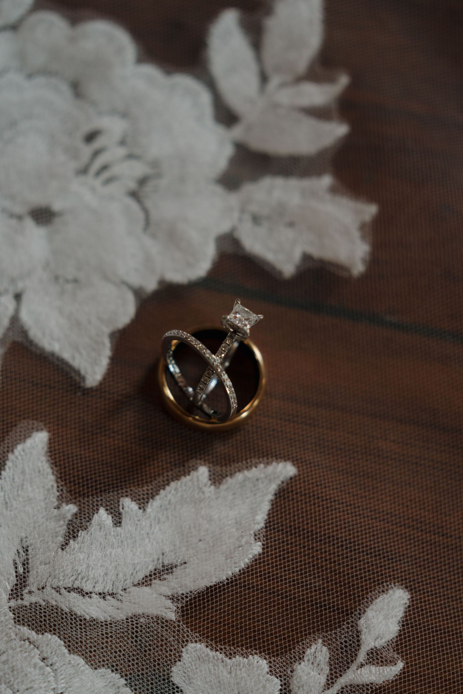 Wedding rings resting on delicate white lace fabric with floral embroidery on a wooden surface.