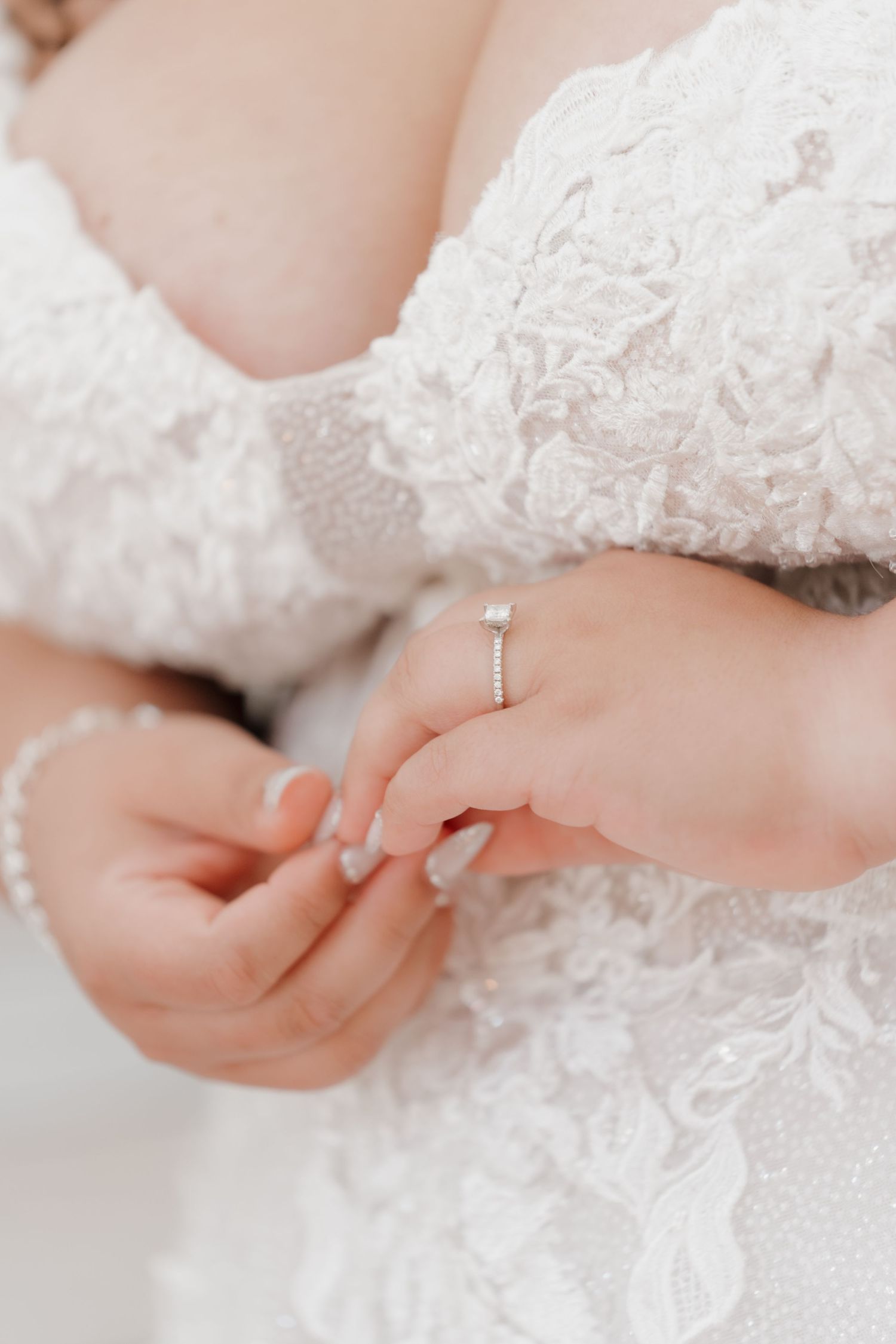 Close-up of bride in lace wedding dress showcasing elegant diamond engagement ring on her finger.