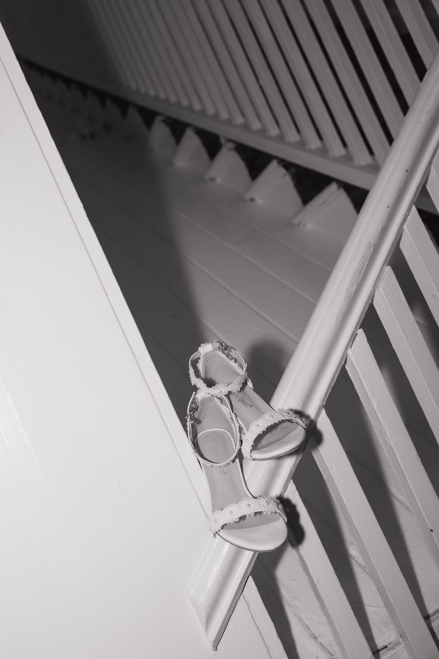 White bridal heeled sandals hanging on staircase railing in black and white wedding photography.