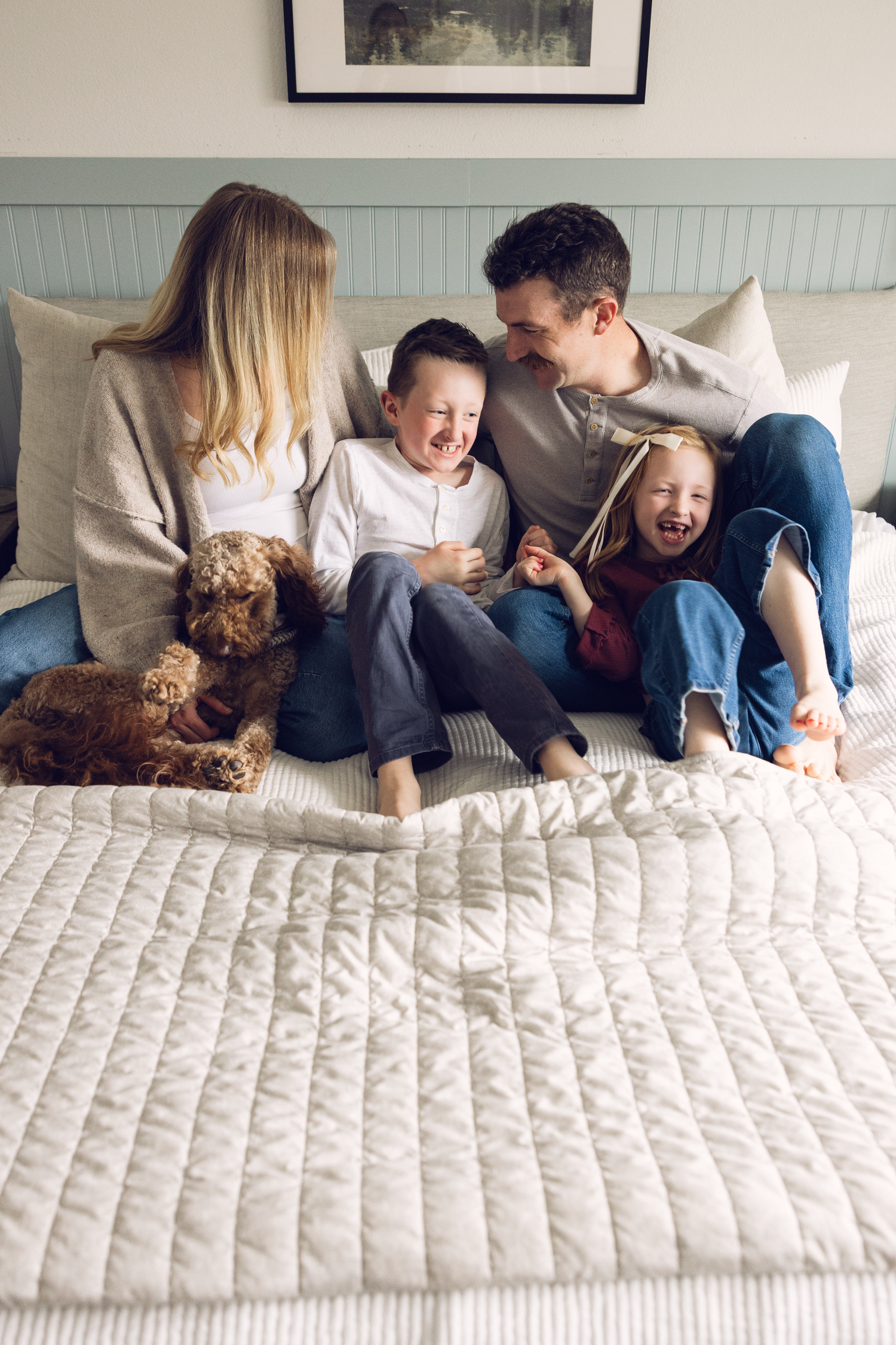 Happy family with two children and a brown dog laughing together on a bed with white bedding.