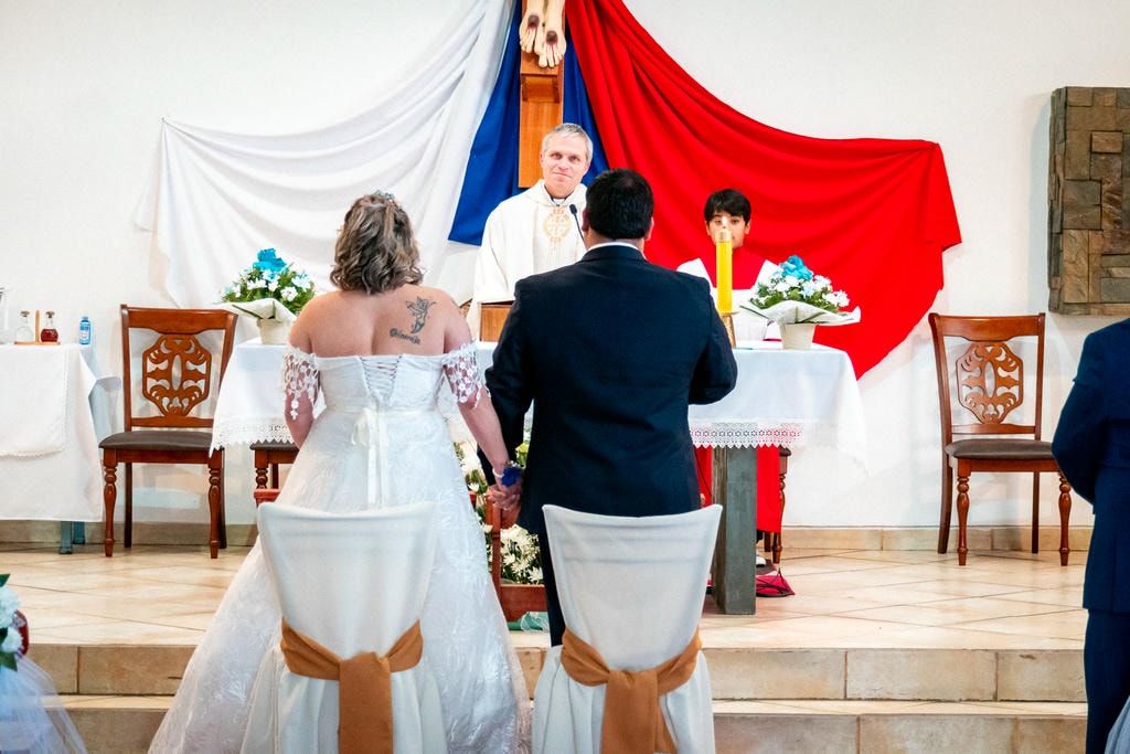 Plano general de los novios de espaldas en el altar junto al cura una toma de reportaje que captura la arquitectura y solemnidad de la boda