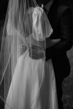 Black and white wedding photo showing delicate bridal veil with beaded trim detail and white wedding dress.