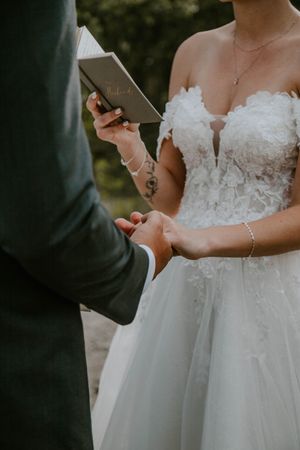 A couple exchanges vows during their wedding ceremony, with the bride holding a book while wearing a lace wedding gown.