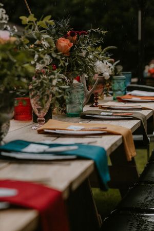 A rustic outdoor table setting with teal and red accents features elegant floral centerpieces and place settings.
