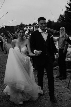 A bride and groom dance together outdoors at their wedding reception, surrounded by guests in black and white.
