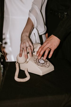 A sequence of hands dialing numbers on a vintage rotary telephone in a dark setting.