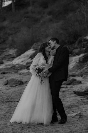 A romantic black and white wedding photo shows a couple sharing a kiss on rocky terrain as the bride holds a bouquet.