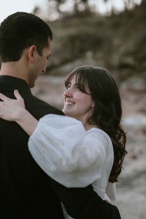 A romantic couple embraces outdoors during a moody photoshoot with soft natural lighting.