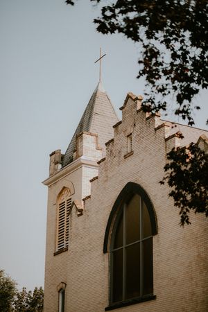 Three identical church steeples with arched windows and crosses on top against a cloudy sky framed by tree branches.