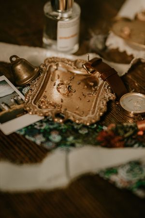 Vintage ornate golden frame with bell and floral pattern sits on dark wooden surface with scattered photographs.