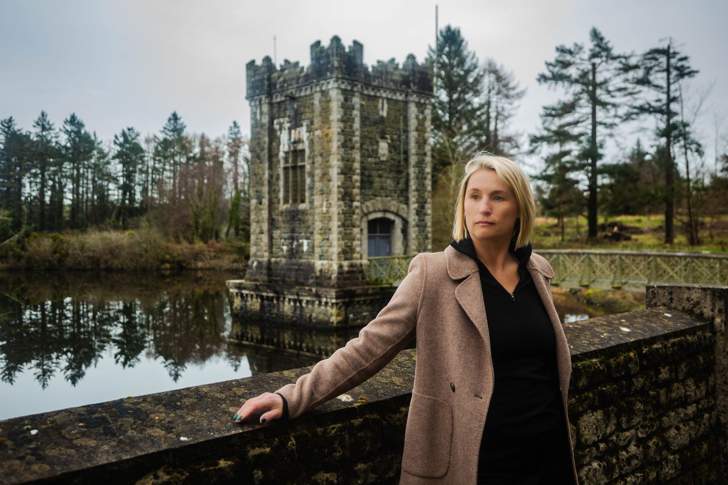 Portrait at Vartry Reservoir with  a Draw Tower, a serene lake  and evergreen trees in the background.