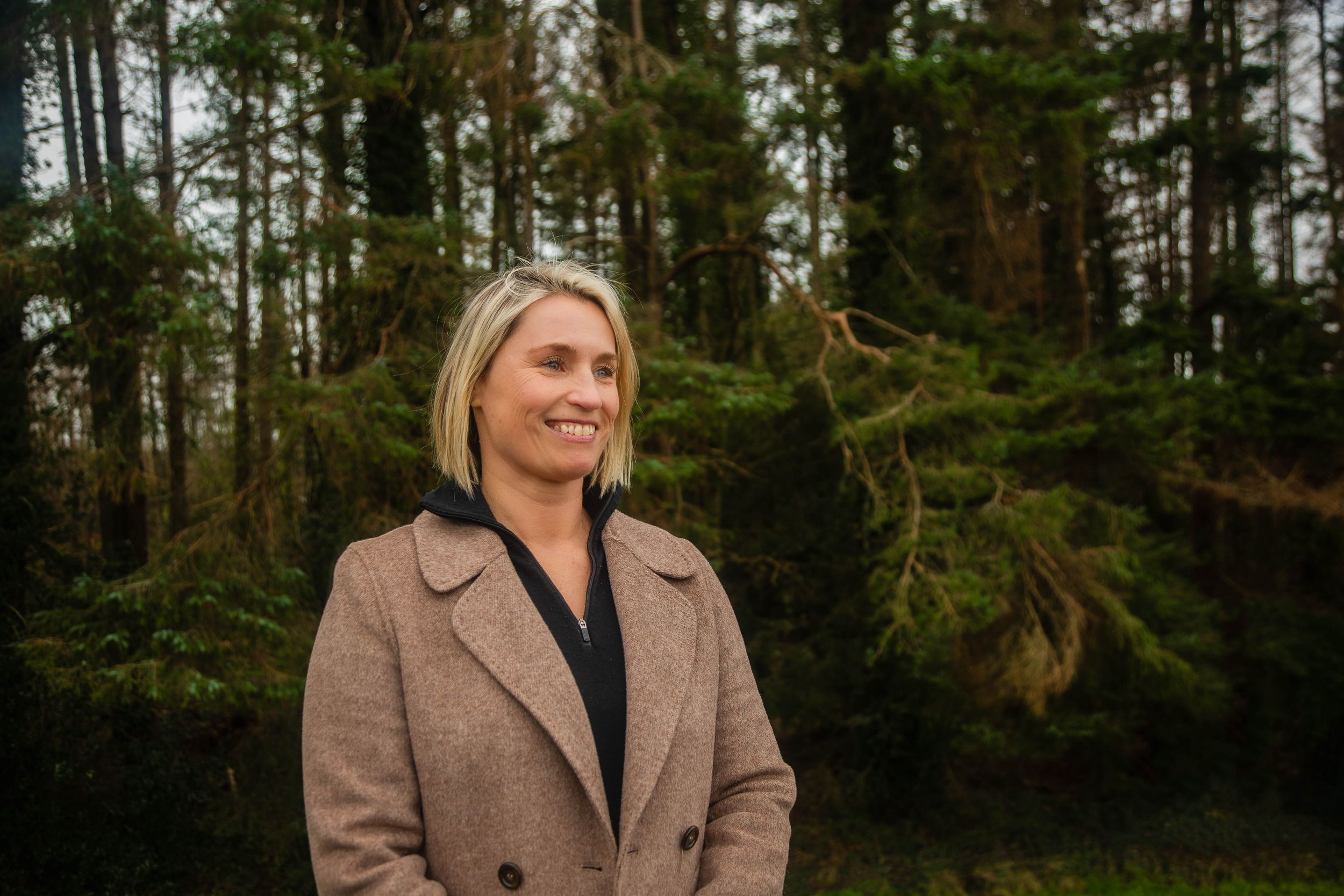 Outdoor portrait session among tall pine trees with moody overcast lighting.
