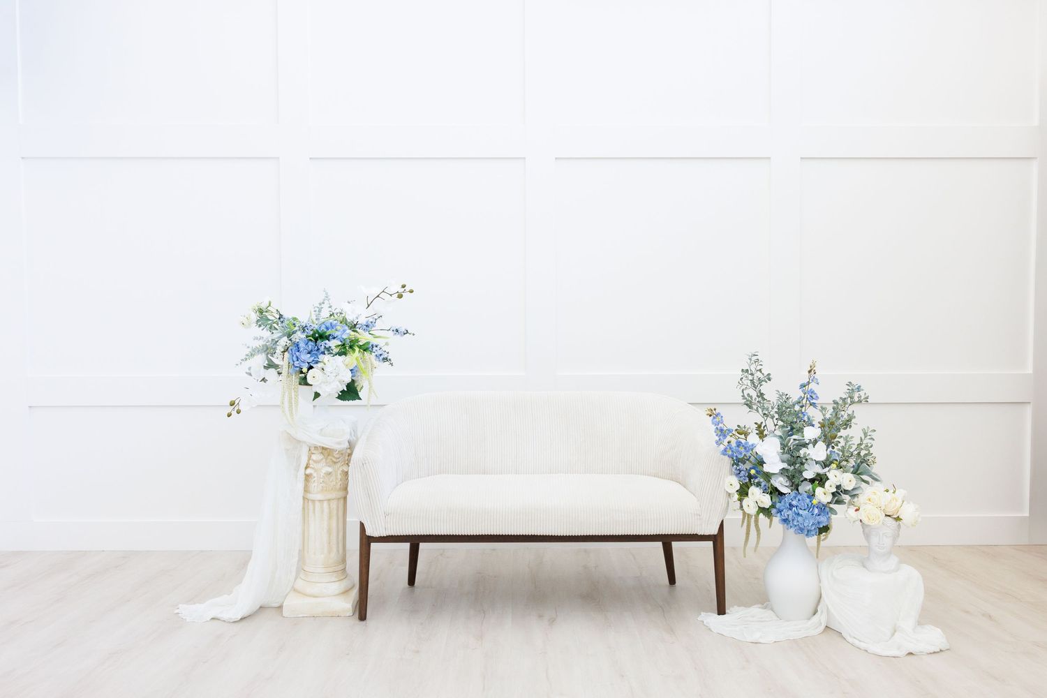A delicate blue floral arrangement sits atop a white bench against a minimalist white wall.