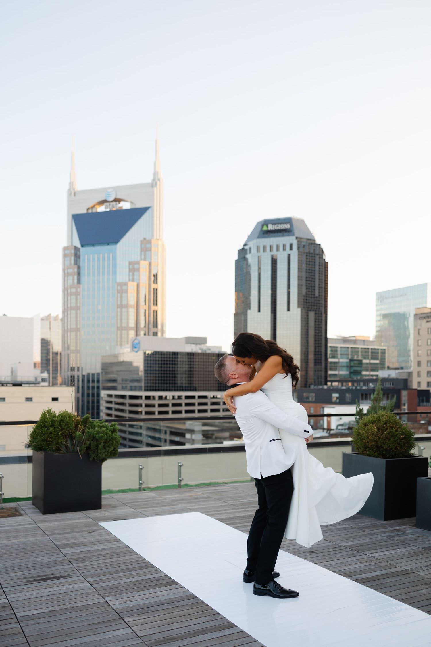 A couple embraces in a romantic dip pose on a rooftop deck with the Nashville skyline in the background.