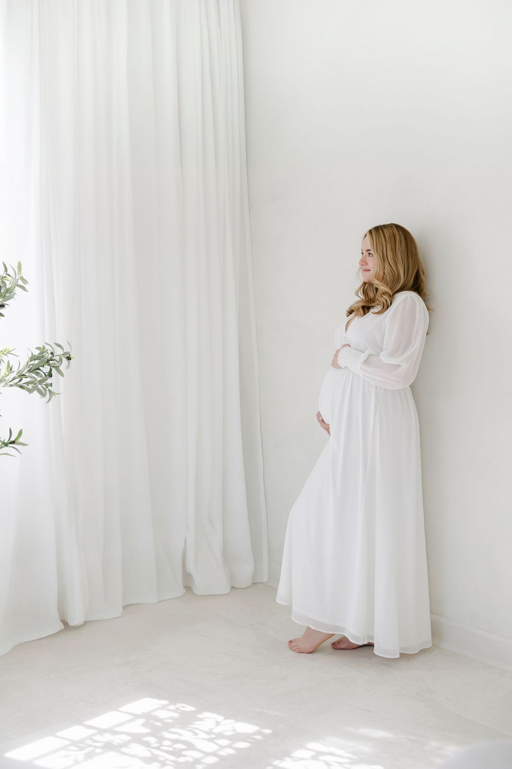 Four artistic photos of someone wrapped in white fabric in a bright minimalist room with white curtains and natural light.