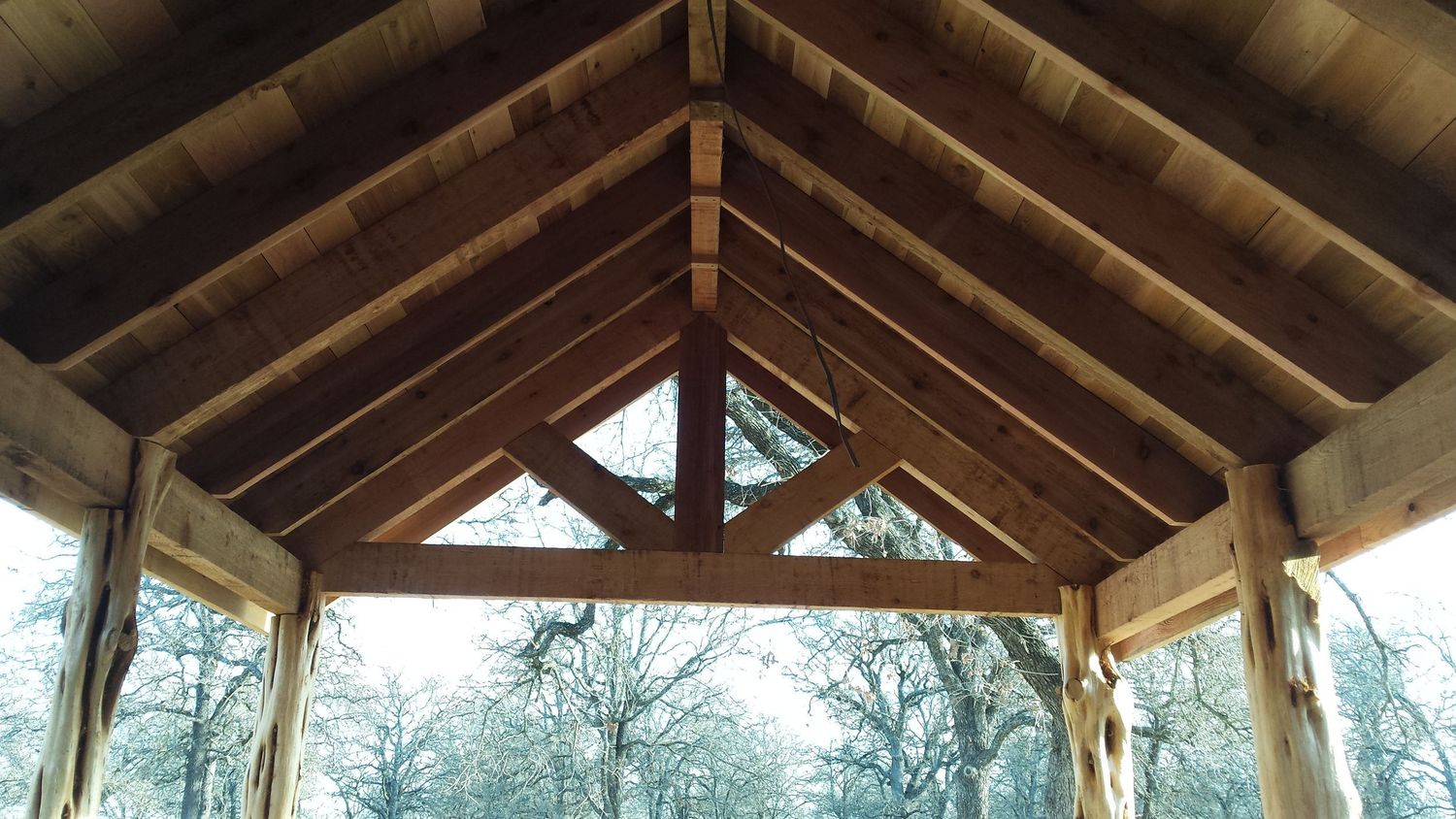 Looking up at wooden beams and rafters in a vaulted ceiling structure.