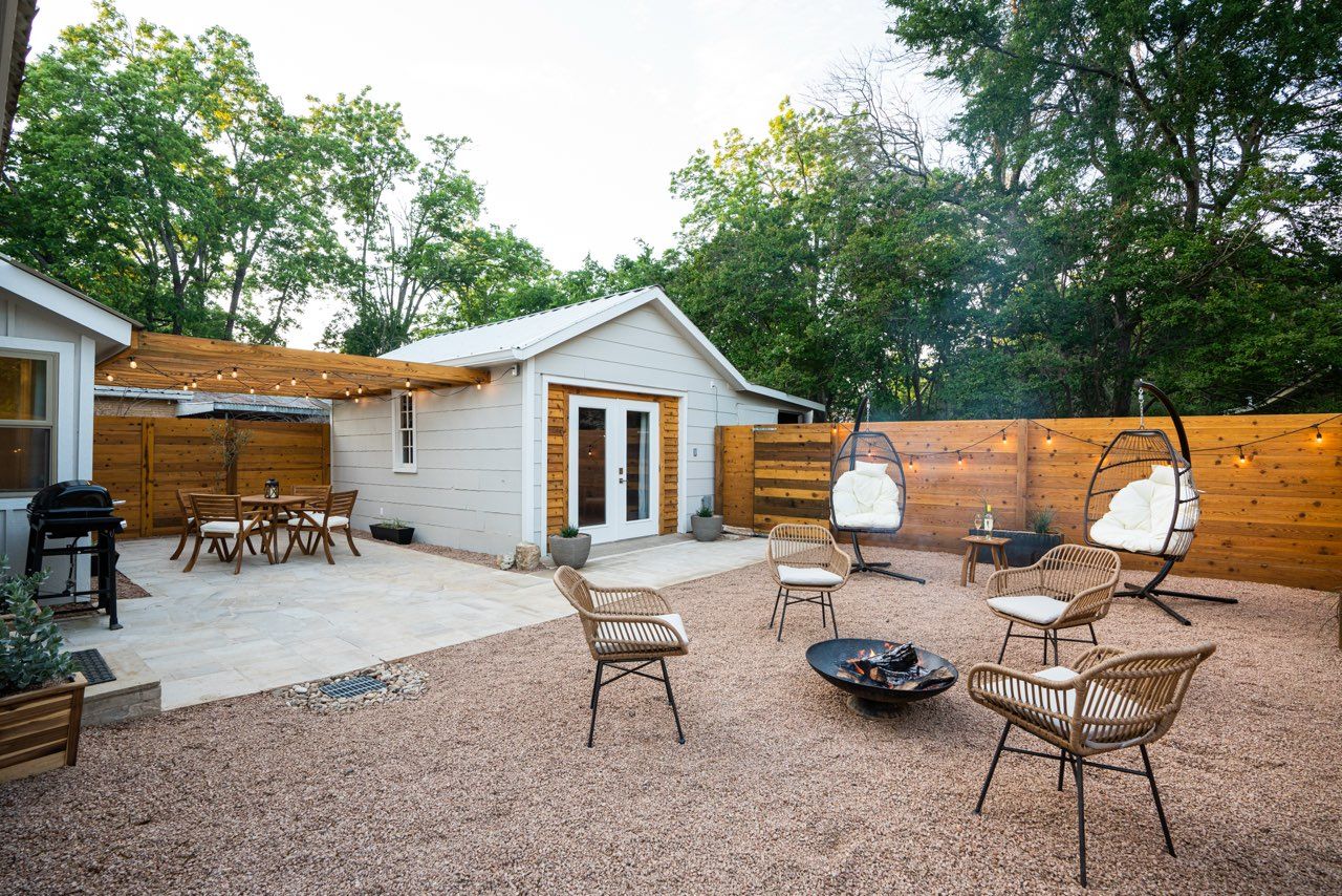 Outdoor patio area with fire pit and multiple seating arrangements surrounded by landscaping.