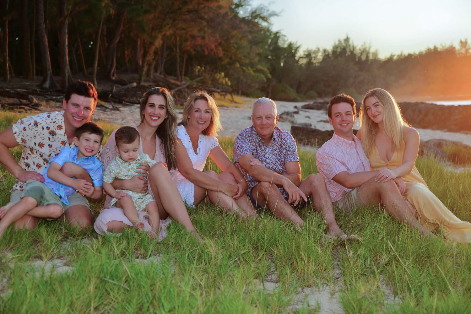 A family relaxes together on grassy ground during golden hour sunset at a scenic outdoor location.