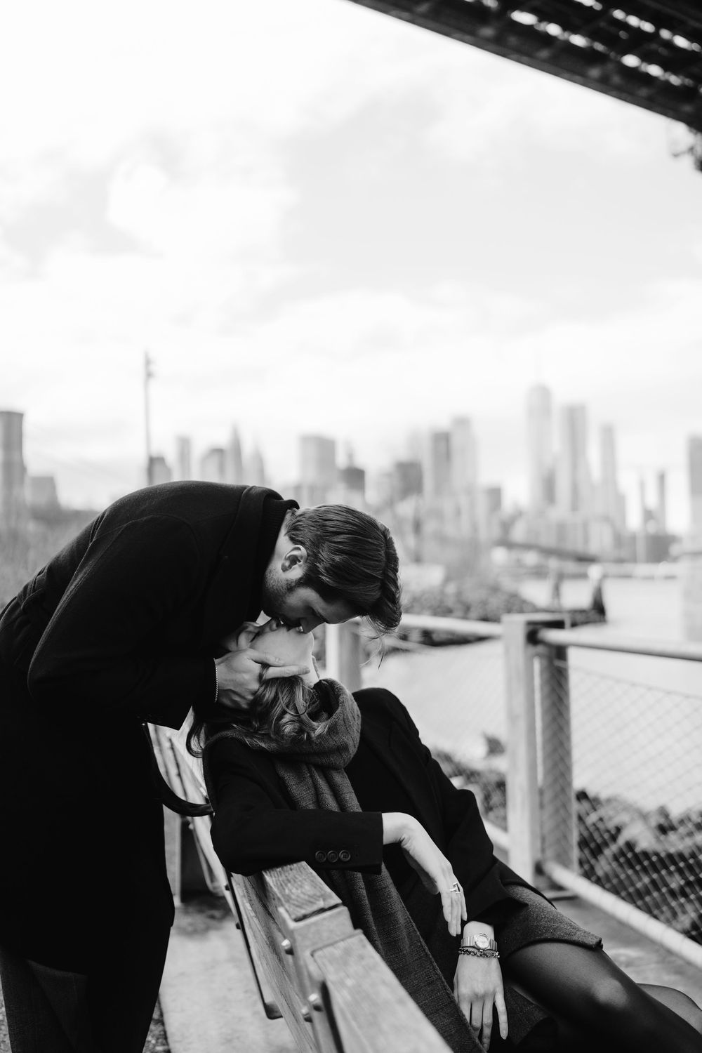 A romantic black and white moment between a couple on a rooftop bench with the city skyline in the background.