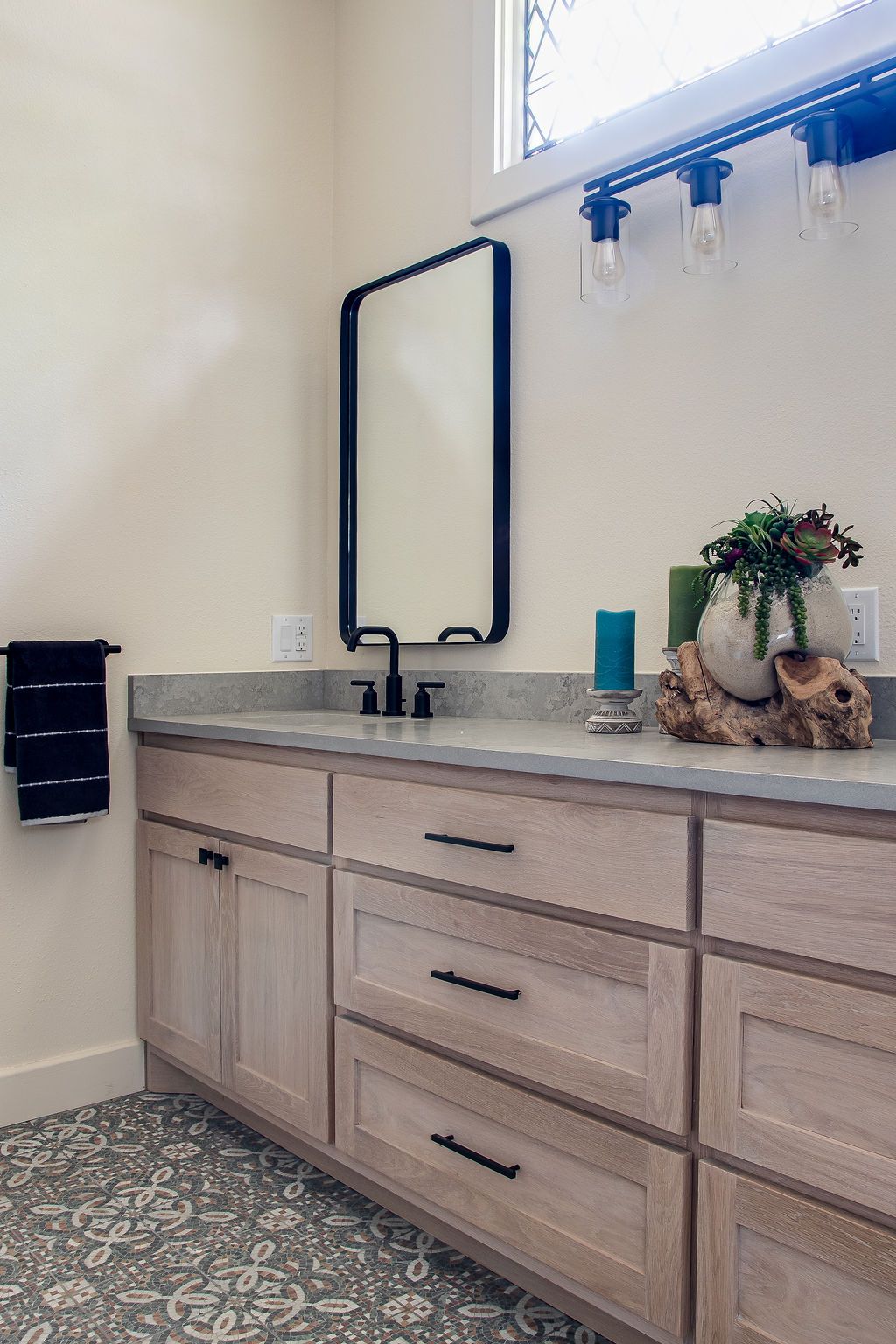 Contemporary bathroom vanity with light wood cabinets and patterned tile flooring.