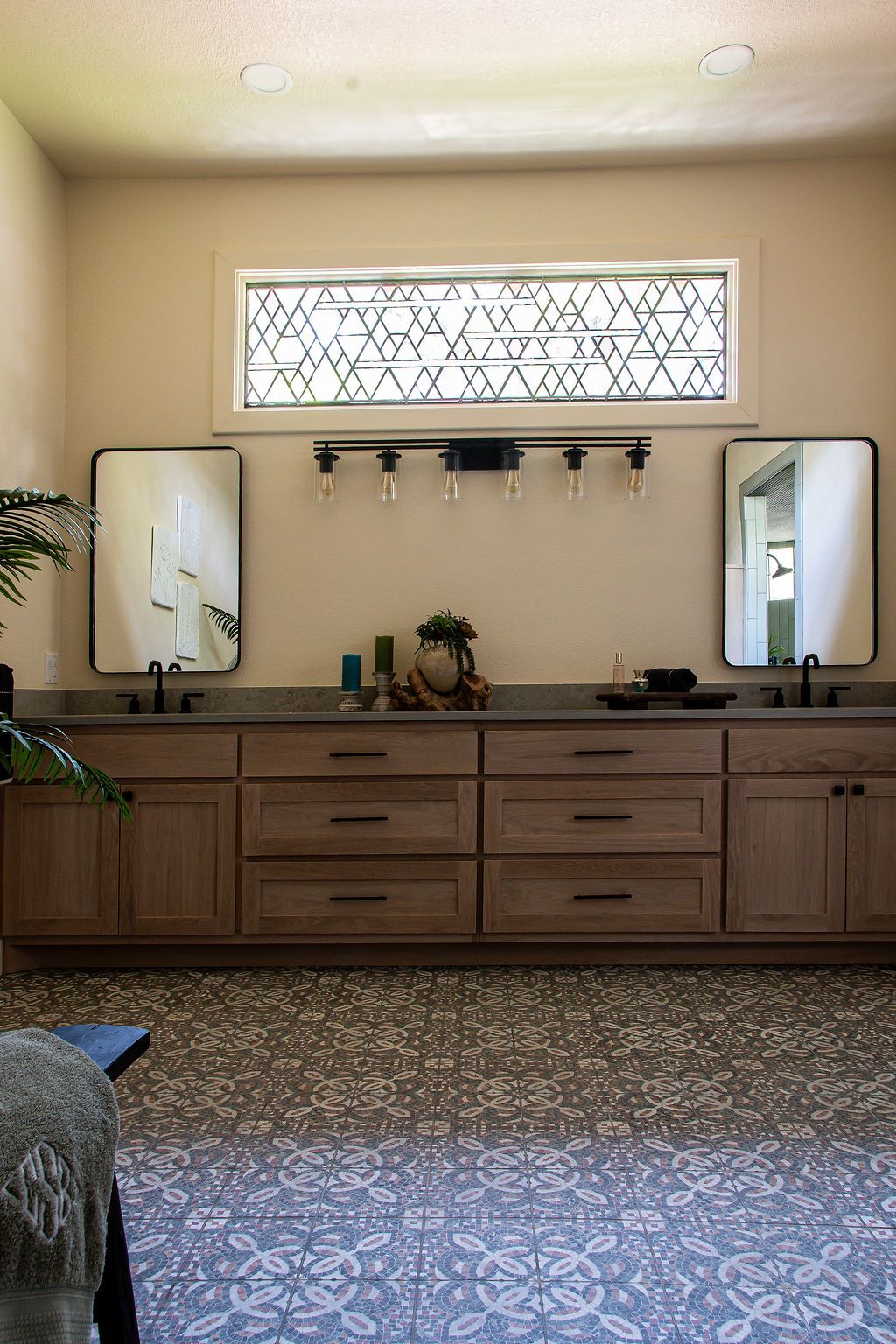 Long bathroom vanity with decorative transom windows and patterned floor tiles.