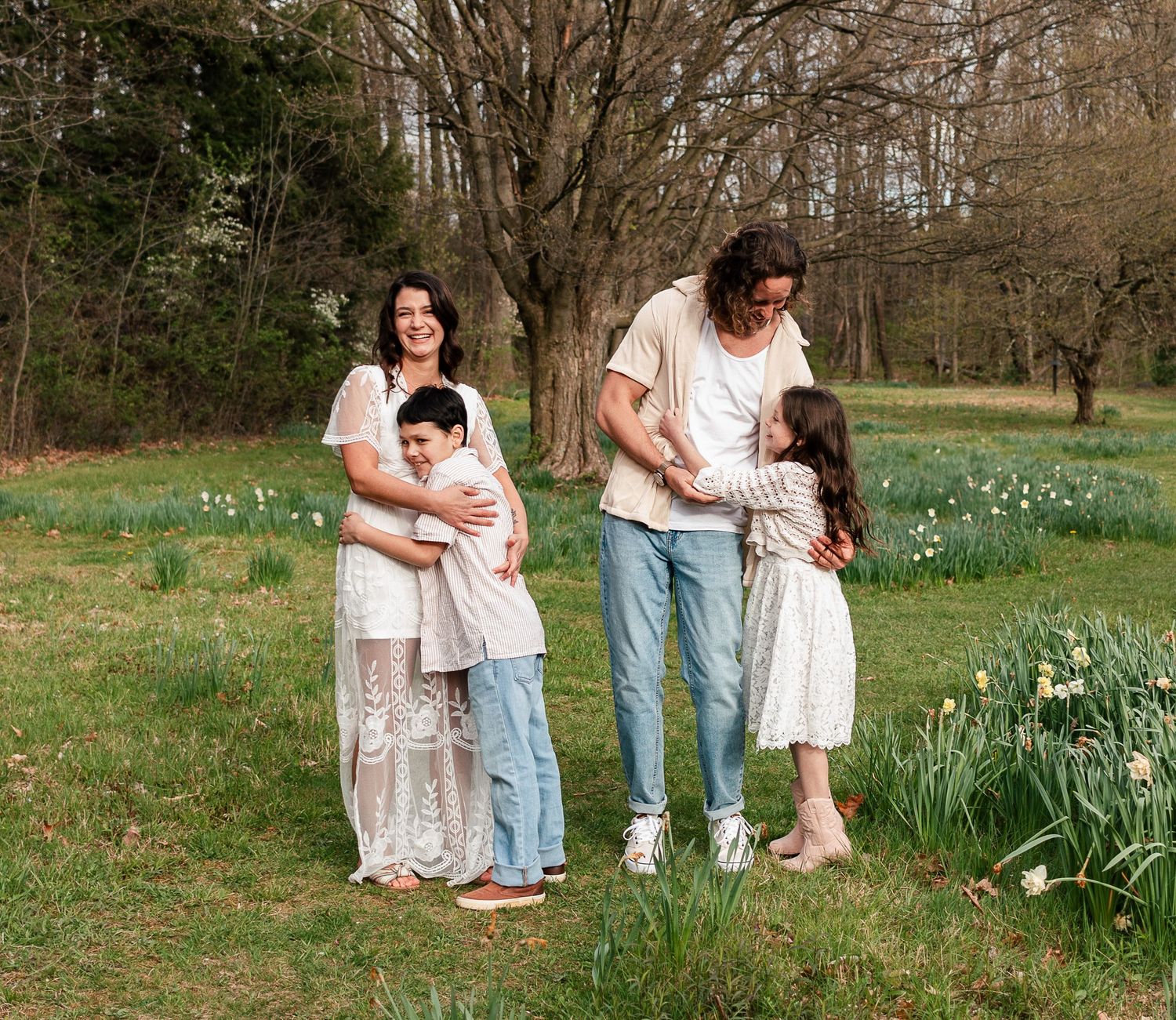 A family stands together in a spring garden with blooming daffodils and bare trees in the background.Family, senior, and wedding photographe