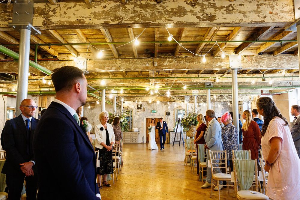 A large industrial event space with exposed brick walls and wooden beams hosts a gathering with tables and guests.