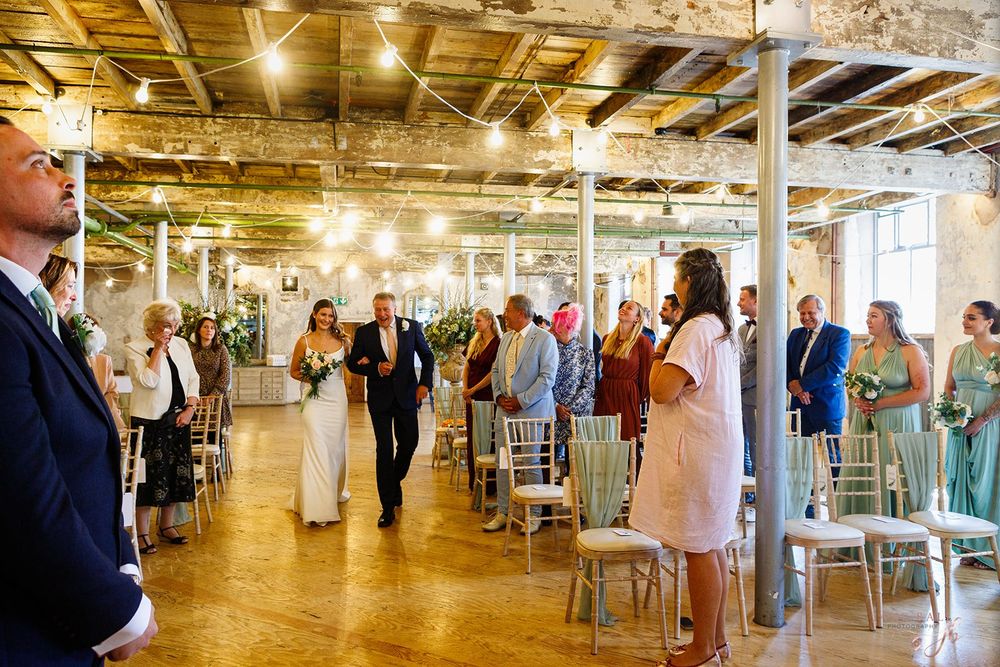 Wedding guests mingle and socialize in an industrial-style venue with exposed ceiling and warm lighting.