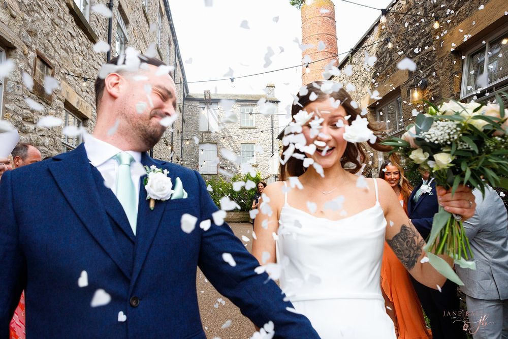 A couple laughs together as confetti falls around them during their wedding celebration.