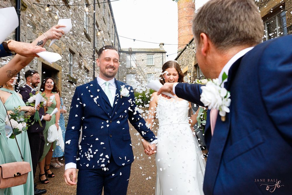 Wedding guests shower newlyweds with confetti outside a stone building during a joyful celebration.