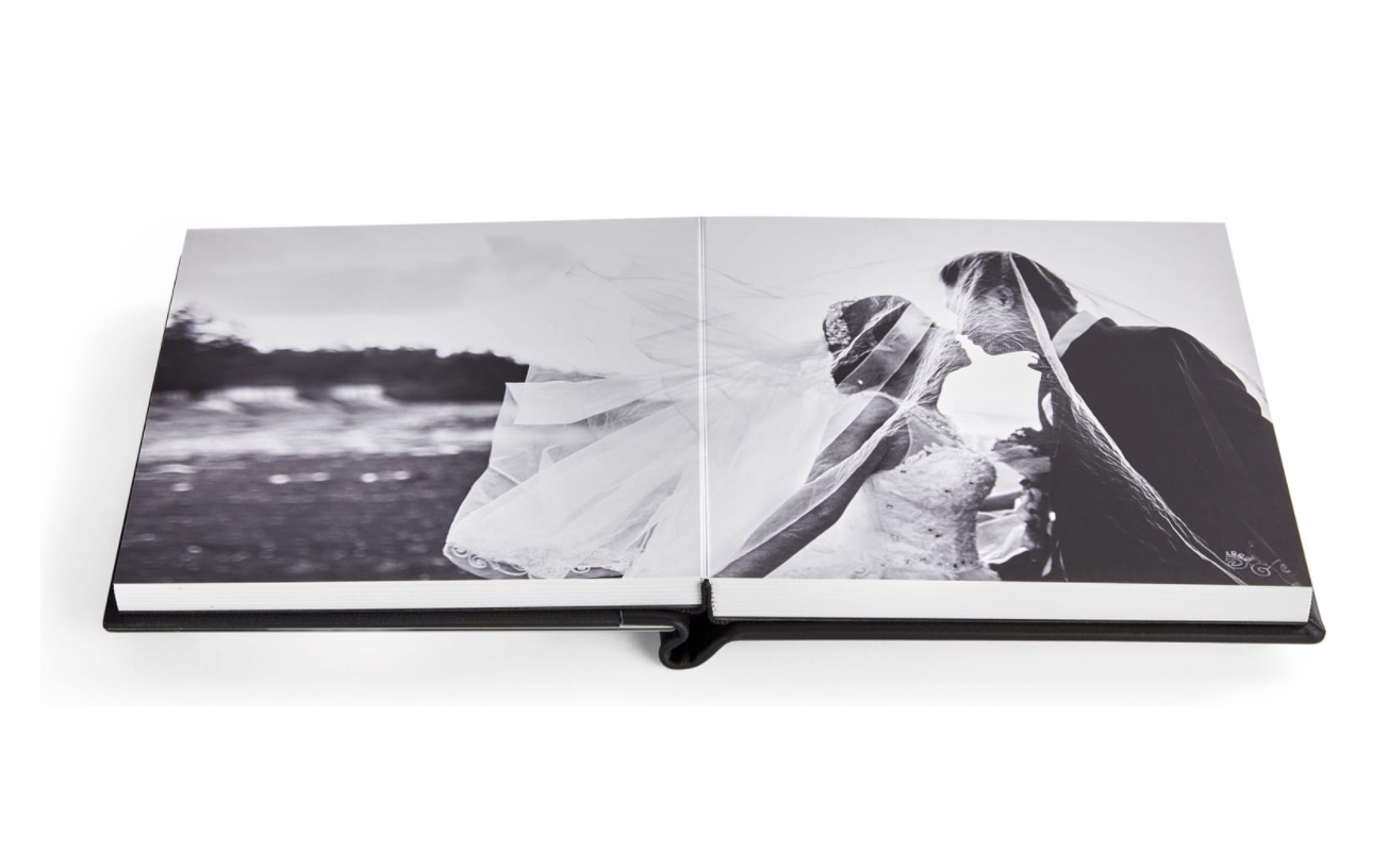 A black and white wedding photo album lies open showing a romantic couple's portrait spread across two pages.