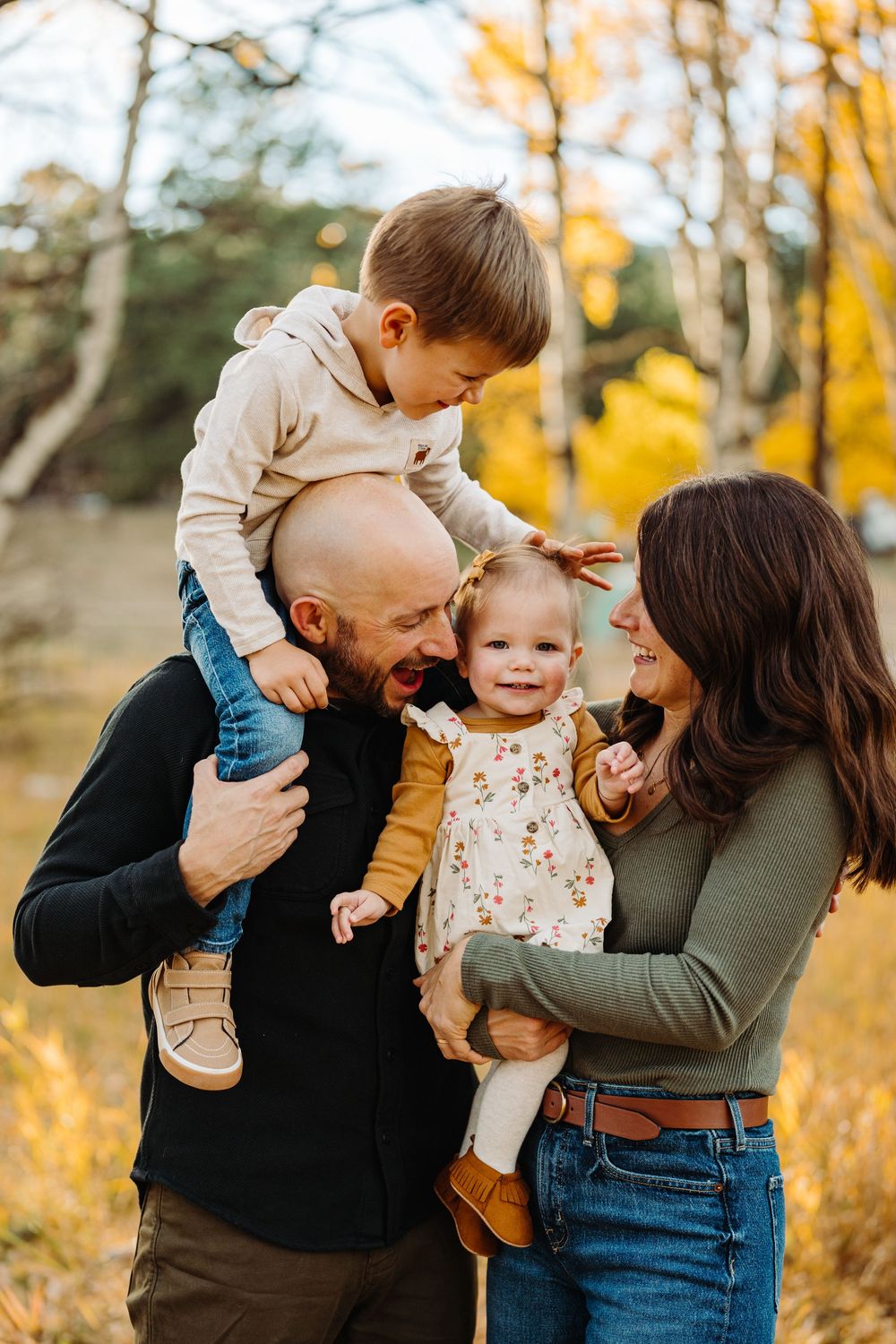 Happy family embraces and shares joyful moments together during fall photoshoot in golden forest setting.